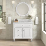 The Lorelai 36-inch Bathroom Vanity Cabinet boasts a white finish with two drawers, a cupboard, a marble countertop, and silver faucet. It sits under a round scalloped mirror with wall sconces and nearby hand towels, while a large window adorns the right.