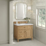 The bathroom features a Lorelai 36 inch Bathroom Vanity Cabinet topped with a white counter and adorned with a vase of flowers. Above, a geometric mirror is hung, complemented by soft floral wallpaper and a window view of lush greenery for a tranquil ambiance.