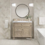 The bathroom showcases the Lorelai 36-inch Bathroom Vanity Cabinet adorned with a white countertop and round mirror. Two pendant lights hang above, towels flank each side, and a vase of flowers sits on the counter, all set against herringbone-tiled walls.
