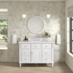 The bathroom showcases the white Lorelai 48 Single Bathroom Vanity Cabinet with drawers and a center cabinet, topped by a round mirror and illuminated by wall sconces. Hand towels hang from round holders on each side, while natural light streams through a window on the right.