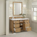 The Lorelai 48 inch Single Bathroom Vanity Cabinet with a white countertop, open drawers, and cabinet doors sits below a large mirror, flanked by two wall sconces and a vase of flowers against floral wallpaper and a nearby window.