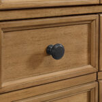 Close-up of the Malibu 36 inch Bathroom Vanity Cabinet - Amber Birch, showcasing its carved wooden drawer front with a round black knob. The natural finish accentuates the grain, and the centrally placed knob casts a soft shadow on the surface.