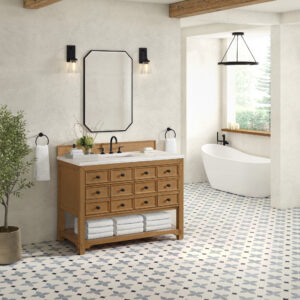 A modern bathroom showcases patterned tile flooring with a Malibu 48 inch Bathroom Vanity Cabinet in Amber Birch, featuring drawers below a large mirror flanked by two wall-mounted lights. A freestanding white bathtub near a window offers views of greenery, while a potted plant enhances serenity.