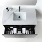 The Matera 36 Inch Wall Mount Bathroom Vanity With Countertop includes a white marble surface, integrated sink, black faucet, open drawer for towels and toiletries, and space on the countertop for bottles next to the sink.