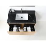 The Matera 48 Inch Wall Mount Bathroom Vanity With Countertop includes a sleek black marble surface, white rectangular sink, and an open wooden drawer, creating a modern, organized space for toiletries, towels, and bottles.