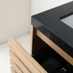 A close-up of the Matera 36 Inch Wall Mount Bathroom Vanity With Countertop highlights its sleek black surface and integrated sink, with a partially open wooden drawer featuring horizontal grooves against white walls in the background.