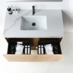 The Matera 36 Inch Wall Mount Bathroom Vanity With Countertop includes a white marble top, built-in sink, black faucet, and an open wooden drawer for organized storage of toiletries and towels.