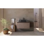 A modern bathroom with beige walls features the Ocala 36 Inch Wall Mount Bathroom Vanity With Vessel Sink, a mirror, potted plant, towel rack, wooden storage unit, an open shower area, and is filled with natural light.
