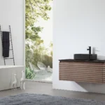 Minimalist bathroom showcasing the Ocala 48 Inch Wall Mount Bathroom Vanity With Vessel Sink, a floating wood vanity, black sink, freestanding white tub, towel ladder, two giraffe figurines, and floor-to-ceiling window with patio view.