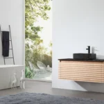 Minimalist bathroom with an Ocala 48 Inch Wall Mount Bathroom Vanity With Vessel Sink, black sink, matte black faucet, freestanding tub, ladder towel rack, and decorative giraffes. Large window overlooks a lush patio with chairs.