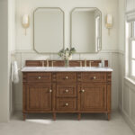 A bathroom features the Lorelai 60 inch Double Bathroom Vanity with two mirrors, gold faucets, wall sconces, and a flower vase atop the counter. Hexagonal tile floors and neutral walls complete the calm, elegant space.