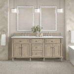 A neutral-toned bathroom features the Lorelai 72 inch Double Bathroom Vanity, two framed mirrors, pendant lights, a flower arrangement, and white towels on racks. Beige herringbone and stone pattern tiles adorn the walls and floors.