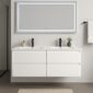 A modern bathroom with a floating white double vanity, two black faucets, a small potted plant, a large backlit mirror, and a towel hanging on a black rod on a light-colored wall.