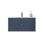 A modern Barcelona 42 Inch Wall Mount Bathroom Vanity features a ribbed navy blue cabinet, a white countertop, a black faucet, and decorative items like a reed diffuser and glass containers.