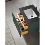 A Barcelona 30 Inch Wall Mount Bathroom Vanity with a black countertop, white sink, green cabinet door, and open wooden drawers holding toiletries sits on a grey floor next to a light textured rug.