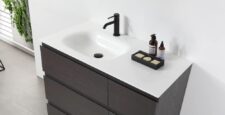 The Rothenburg 42 Inch Freestanding Bathroom Vanity has a white countertop, integrated sink, matte black faucet, soap dish with three soaps, two bottles, and a plant beside a white wall.