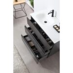 A Rothenburg 42 Inch Freestanding Bathroom Vanity with a white sink, black faucet, and three open drawers filled with towels and toiletries stands on a gray tiled floor beside a beige rug.