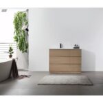 A modern, minimal bathroom features a Rothenburg 42 Inch Freestanding Bathroom Vanity, gray rug, and freestanding bathtub by a window with a leafy plant. The walls are white and the floor is gray tile.