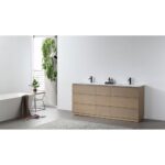 Modern bathroom with a Rothenburg 72 Inch Freestanding Vanity and black faucets, a white freestanding bathtub, side table with towels, tall green plant by the window, minimalist decor, and gray flooring.