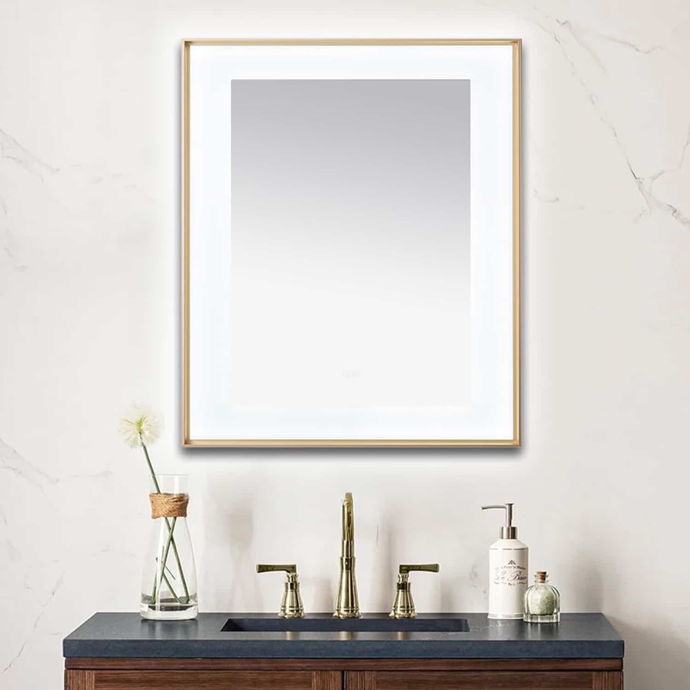 A bathroom vanity with a dark countertop, gold faucet, soap dispenser, and a single flower in a vase sits below the Lexington 30 inch x 36 inch LED Lighted Slim Frame Mirror on a light marble wall.