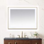A Lexington 48 inch x 36 inch LED Lighted Slim Frame Mirror with a thin gold frame hangs above a dark wood vanity with black countertop, gold faucet, soap dispenser, and small floral arrangement against a light marble-veined wall.