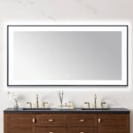 A modern bathroom features the Lexington 72 inch x 36 inch LED Lighted Slim Frame Mirror above a double sink vanity with brass faucets, wooden cabinets, and toiletries neatly arranged on the countertop.