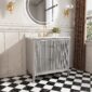 A modern bathroom features the Aveline 36 Inch Freestanding Bathroom Vanity with Top, gray fluted front, gold faucet, round mirror, wall sconces, small flower vase, black-and-white checkered tile floor, white wainscoting, and a window.
