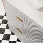 The Aveline 36 Inch Freestanding Bathroom Vanity With Top features vertical ridges, gold handles, and a white marble countertop, and is shown on a striking black and white checkered tile floor.
