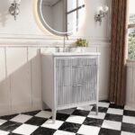 The Aveline 30 Inch Freestanding Bathroom Vanity With Top features a ribbed gray cabinet, white countertop, faucet, round backlit mirror, wall sconces, small vase of flowers, and a black-and-white checkered tile floor.
