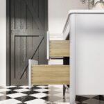 The Aveline 30 Inch Freestanding Bathroom Vanity With Top features two wooden drawers open, set on a black and white checkered tile floor beside a dark barn-style door and a chrome faucet.