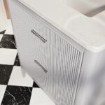 A close-up of the Aveline 30 Inch Freestanding Bathroom Vanity With Top highlights vertical grooves on the drawers, metal handles, and a white marble countertop. The floor showcases a black and white checkered tile pattern.