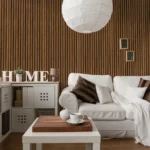 A cozy living room with a white sofa, brown and white cushions, a blanket, a small coffee table with tea set, “HOME” letters, modern shelving, and the Acoustic Interior Wall Panel as an elegant accent.