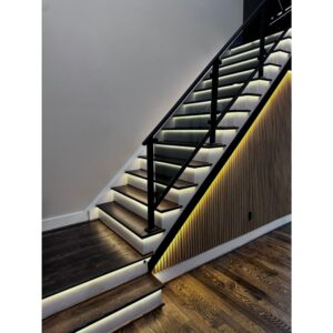Modern staircase with dark wooden steps, black railing, and built-in LED strip lighting along the edges and beneath the railing, highlighting the textured wood panel wall and polished wood floor.