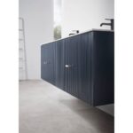 Modern bathroom with a Barcelona 60 Inch Wall Mount Double Bathroom Vanity With Top in navy blue, enhanced by vertical grooves, brass handles, and black faucets. Light gray floor and large window complete the bright, minimalist style.