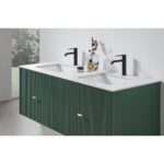 The Barcelona 60 Inch Wall Mount Double Bathroom Vanity With Top features dark green, vertically grooved drawers, a white countertop, two black faucets, and minimal decor. A window offers views of greenery that enhance the vanity’s modern style.