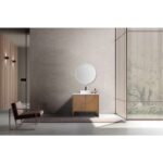 A minimalist bathroom showcases the Celle 36 Inch Bathroom Vanity With Vessel Sink, paired with a round mirror and light grey wall. A modern chair on a rug complements the look, while tall vertical slats frame views of greenery outside.