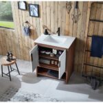 The Lyon 30 Inch Bathroom Vanity with Top includes a white sink, black faucet, and dual open doors showing shelves with jars and towels, set by a wood-paneled wall alongside a window and stool holding toiletries.