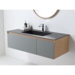 The Oslo 48 Inch Wall Mount Bathroom Vanity has a gray countertop, built-in sink, light wood accents, and comes with a soap dispenser and bottle on the surface. A round mirror is partially visible above the vanity.