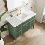 The Aveline 48 Inch Freestanding Bathroom Vanity With Top features a green finish, gold handles, and a white marble countertop. Gold faucet, rectangular sink, mirror, small plant, soap dispenser, and light wood flooring complete the look.