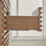 A close-up side view of a wooden drawer in the Linea 48 Inch Wall Mounted Bathroom Vanity, partially open to reveal its modern slatted design and dovetail joints, with sunlight streaming through a window in the background.