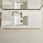 Sleek bathroom sink with a rectangular white countertop, gold faucet, and square basin seen from above—part of the stylish Linea 48 Inch Wall Mounted Bathroom Vanity. The edge of a mirror appears at the top of the image.