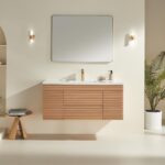 Minimalist bathroom featuring the Linea 48 Inch Wall Mounted Bathroom Vanity, a rectangular mirror, modern brass faucet, two wall sconces, a small wooden stool with books, and a potted plant against a light beige wall.