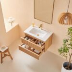 Minimalist bathroom featuring the Linea 30 Inch Wall Mounted Bathroom Vanity with a white sink, gold faucet, open drawers with toiletries, wall mirror, potted plant, wooden stool, pendant light, and a vase of white flowers on a ledge.
