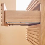 Close-up side view of the Linea 30 Inch Wall Mounted Bathroom Vanity with a partially opened drawer, displaying its metal sliding mechanism and grooved handles against a softly lit beige background.