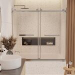 A modern bathroom featuring the Tub Door Double Sliding Frameless, terrazzo wall tiles, built-in shelf with potted plants, a round white sink with wooden accents, and a towel rack and toiletries on the right.