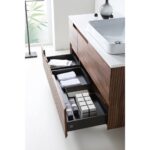 The Orsa 48 Inch Wall Mount Bathroom Vanity With Vessel Sink offers modern style with open drawers for neatly folded towels and boxes, vertical wood paneling, and a sleek vessel sink. Natural light streams in through a frosted window.