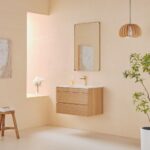 Minimalist bathroom with a Linea 30 Inch Wall Mounted Bathroom Vanity, white sink, gold faucet, rectangular mirror, wooden stool, potted plant, hanging wood light, sunlight through the window, and a vase of flowers.