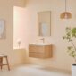 Minimalist bathroom with a Linea 30 Inch Wall Mounted Bathroom Vanity, white sink, gold faucet, rectangular mirror, wooden stool, potted plant, hanging wood light, sunlight through the window, and a vase of flowers.
