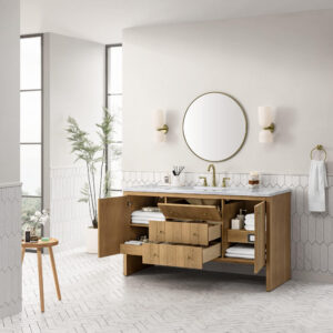 Modern bathroom with a wooden vanity, open drawers and cabinets displaying towels and toiletries, a round mirror, wall sconces, a towel ring, and a potted plant by large windows. White tile and herringbone floor complete the space.