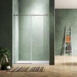 A modern bathroom with sage green textured walls, a glass sliding shower door, a striped rug on a wooden herringbone floor, a small potted plant, and a white ladder shelf holding folded towels.